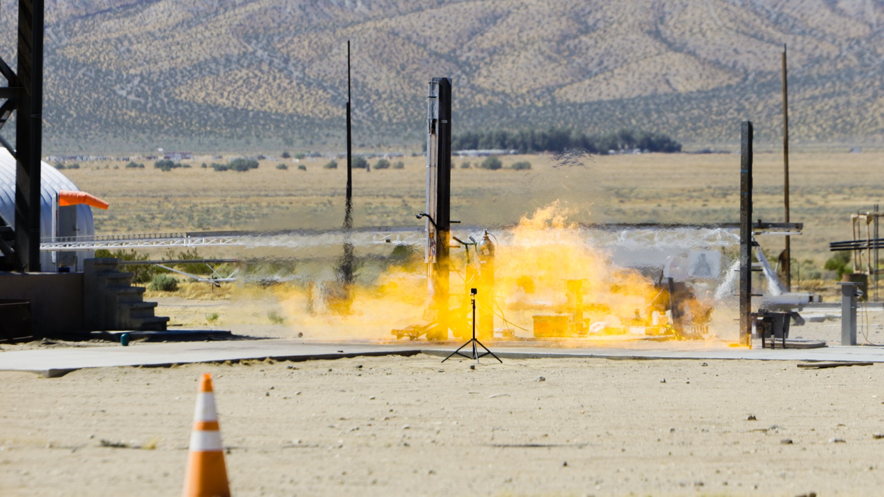A hard start engulfs the test stand in an orange fireball with desert mountains behind